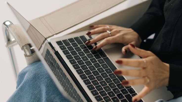 A woman typing on a laptop balanced on her lap, hands resting on the keyboard mid-sentence